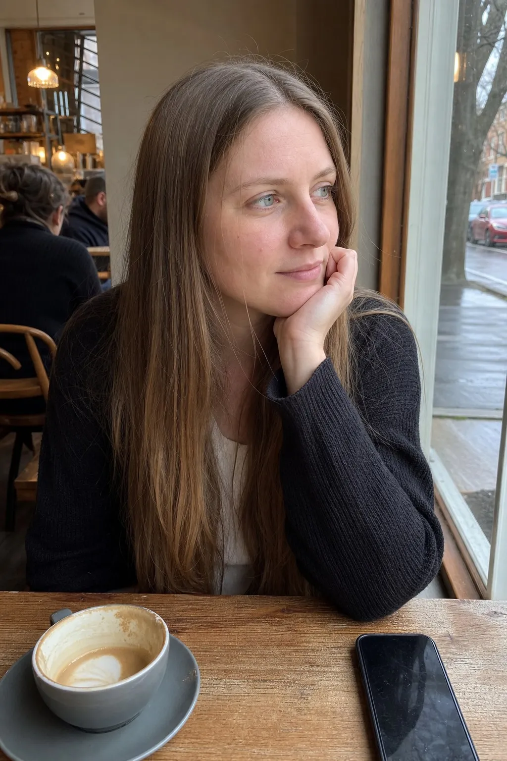 A woman at a cafe window before and after long layers with curtain bangs - before