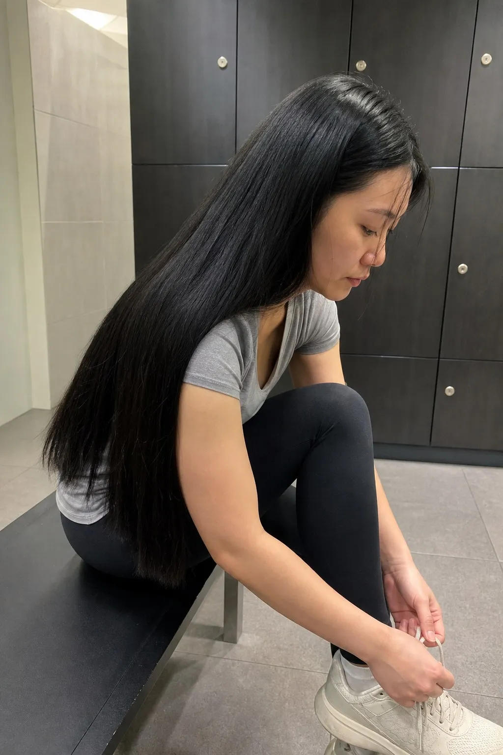 A woman tying her shoes in a gym changing room before and after long layers with thinned ends - before