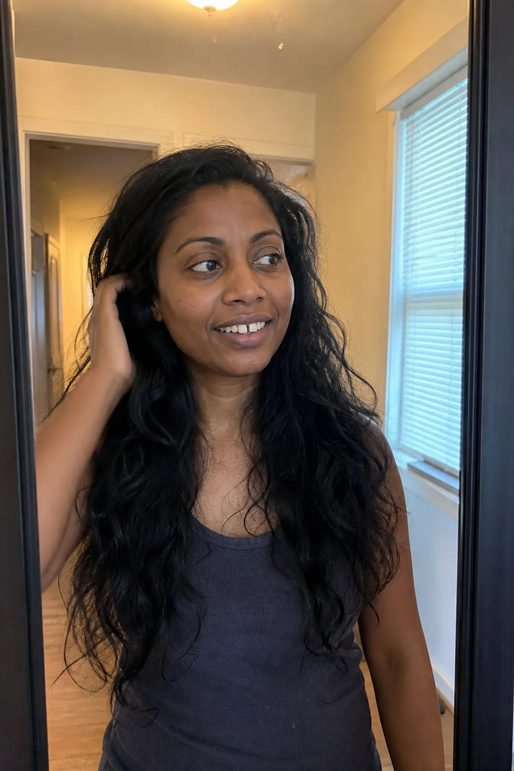 A woman in a hallway mirror before and after a butterfly cut - before